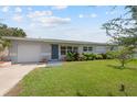 Single story home with gray exterior, showing garage door, blue door, landscaping, manicured lawn and multi-pane windows at 5961 41St N Ave, St Petersburg, FL 33709