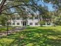Traditional white home with black shutters, mature trees, circular driveway, and second story balcony at 12433 Kelso Rd, Thonotosassa, FL 33592