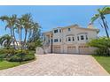 Elegant home featuring a brick driveway, three-car garage, and landscaped front yard with tropical trees at 1156 2Nd S Ave, Tierra Verde, FL 33715