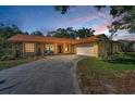 Charming single-story home featuring a stone facade, lush landscaping, and a long driveway leading to an attached garage at dusk at 3041 Oak View Dr, Palm Harbor, FL 34684