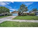 Single-story home featuring lush landscaping, a large palm tree, and a two-car garage at 1281 Amberlea E Dr, Dunedin, FL 34698