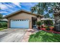 Single-story home featuring a large palm tree, landscaped front yard and a two-car garage at 1281 Amberlea E Dr, Dunedin, FL 34698