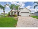 Attractive home with manicured lawn, palm trees, and a brick driveway leading to an attached two-car garage at 11904 Greenchop Pl, Riverview, FL 33579