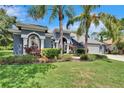 Charming blue home featuring a three-car garage, well-manicured lawn, and lush landscaping at 27440 Cedar Park Ct, Wesley Chapel, FL 33544