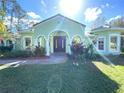 Beautiful single-story home boasts a lush front lawn, arched entryway with double doors, and verdant landscaping at 27752 Ravens Brook Rd, Wesley Chapel, FL 33544