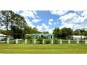 Charming single-story home with a well-manicured lawn and a stylish black fence, nestled among lush trees under a partly cloudy sky at 27752 Ravens Brook Rd, Wesley Chapel, FL 33544