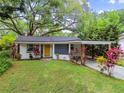 Charming single-story home with mature trees, colorful plants, carport, and bright yellow front door at 1311 W Perdiz St, Tampa, FL 33612