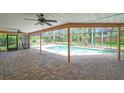 Covered patio with brick pavers, ceiling fans, and views of a sparkling screened-in pool and tropical landscaping at 1695 Cinnamon Ln, Dunedin, FL 34698