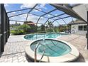 A covered pool and hot tub surrounded by brick pavers with an outdoor screened enclosure at 1286 Stony Brook Ln, Dunedin, FL 34698