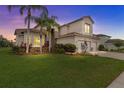 Stunning two-story home with a three-car garage, lush landscaping, and mature palm trees at sunset at 2724 Coco Palm Cir, Wesley Chapel, FL 33543