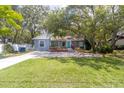 Quaint one-story home featuring mature trees, vibrant green grass, and a welcoming red railing entrance at 715 W 109Th Ave, Tampa, FL 33612