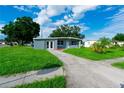 A gray home features a green lawn, mature trees and a long sidewalk leading up to the door at 8502 Grapefruit Ave, Tampa, FL 33619