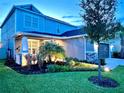 Well-lit two-story home featuring a lush lawn, manicured landscaping, and a cozy front porch at 33560 Castaway Loop, Wesley Chapel, FL 33543