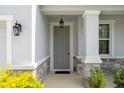 Covered front porch featuring stone accents, classic lighting, and a gray front door at 13919 Wineberry Dr, Dade City, FL 33525