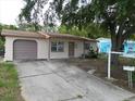 Charming single-story home with a driveway, attached garage, and a mature shade tree in the front yard at 9927 Woodridge Ct, Port Richey, FL 34668