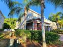 Exterior view of a two-story townhome featuring red brick accents and mature tropical landscaping under a sunny, clear sky at 1427 Hillview Ln, Tarpon Springs, FL 34689