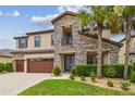 Charming two-story home with a stone facade, covered entry, and vibrant green landscaping with palm trees at 21797 Briske Morning Ave, Land O Lakes, FL 34637