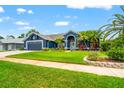 Inviting blue home with well-manicured lawn, colorful flowers, and palm trees under a clear sky, showcasing curb appeal at 28390 Openfield Loop, Wesley Chapel, FL 33543