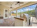 Outdoor kitchen and grill area with ceiling fans and view of the screened pool and green space at 1191 Darlington Oak Ne Dr, St Petersburg, FL 33703