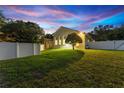 Backyard at dusk with large grassy area, white fencing, and covered patio outside of a beautiful home at 10310 Carroll Cove Pl, Tampa, FL 33612