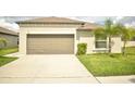 Beige single-story home featuring a two-car garage, palm trees, and a driveway at 16623 Carlton Pond St, Wimauma, FL 33598