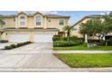 A two-story yellow townhome features a two-car garage and lush landscaping along the driveway and front yard at 3484 Primrose Way, Palm Harbor, FL 34683
