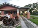 Side view of a house with a covered porch, driveway, mature landscaping, and charming brickwork at 9907 Maggie St, Gibsonton, FL 33534