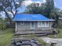 Exterior view of a one-story home with gray siding, a blue tarp on the roof, and a small front deck at 1105 E Ellicott St, Tampa, FL 33603