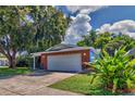 Side exterior view showing a red brick home with a two-car garage and lush trees at 13029 111Th Ln, Largo, FL 33778