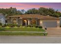 Charming single-story home at dusk featuring a well-manicured lawn, arched windows and a brick-paved driveway at 14228 Teasdale Ave, Hudson, FL 34667