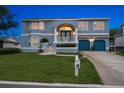 Two-story blue home with a well-manicured lawn, blue garage doors, and a welcoming front porch at twilight at 316 Hillpoint Dr, Palm Harbor, FL 34683