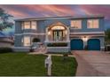 Two-story blue home with a well-manicured lawn, blue garage doors, and a welcoming front porch at sunset at 316 Hillpoint Dr, Palm Harbor, FL 34683