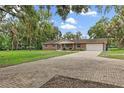 Paver driveway leads to a traditional-style brick home, enhanced by mature trees and lush landscaping at 11029 Clay Pit Rd, Tampa, FL 33610