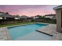 Inviting swimming pool with brick trim and fenced backyard with green grass and neighborhood views at dusk at 5916 Tulip Flower Dr, Riverview, FL 33578