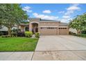 One story tan home with three car garage, red front door, and beautiful landscaping at 32624 Summerglade Dr, Wesley Chapel, FL 33545