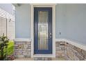 Stylish front door with glass panel, complemented by stone accents and neutral wall color at 10580 Gliding Eagle Way, Land O Lakes, FL 34638