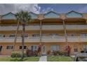 A tan condominium building with palm trees, balconies, and colorful plants sits beneath a partially cloudy sky at 2466 Ecuadorian Way # 32, Clearwater, FL 33763