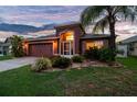 Evening view of single-story home featuring a well-maintained lawn and an attached two-car garage at 31244 Baclan Dr, Wesley Chapel, FL 33545