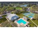 Aerial view of a community clubhouse, swimming pool, tennis courts, and surrounding greenery at 12801 Castle Oaks Dr, Hudson, FL 34669