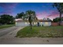 Charming home featuring a well-manicured front yard, a palm tree, and an attached two-car garage, at dusk at 8445 Angela Ct, Zephyrhills, FL 33541