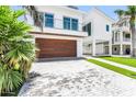 Modern two-story home with a wood garage door, landscaped yard and light brick driveway at 905 Bay Point Dr, Madeira Beach, FL 33708