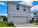 Two-story home with a two-car garage, attractive landscaping, and gray exterior at 13648 Whiskey Daisy Dr, Dade City, FL 33525