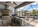 Outdoor kitchen under screened enclosure with stainless steel appliances, bar, and sink at 12415 Hitching St, Odessa, FL 33556