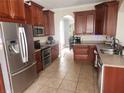 Spacious kitchen featuring tile floors, stainless steel appliances, rich brown cabinets, and granite countertops at 1753 Open Field Loop, Brandon, FL 33510