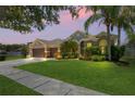 Beautiful home at dusk featuring a well-manicured lawn, a three-car garage, and mature landscaping, showcasing curb appeal at 12801 Stanwyck Cir, Tampa, FL 33626