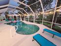 An inviting screened-in pool area with lounge chairs, illuminated by string lights at dusk at 18093 Ohara Dr, Port Charlotte, FL 33948