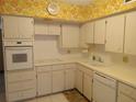 Kitchen with white appliances and cabinets, white countertops, and vintage yellow floral wallpaper at 2459 Franciscan Dr # 29, Clearwater, FL 33763