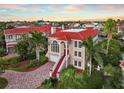 Elegant two-story home boasting a striking red tile roof, red door, grand entrance staircase, and lush tropical landscaping at 6107 Marbella Blvd, Apollo Beach, FL 33572