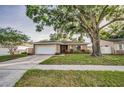 Inviting single-story home with a large tree, a well-kept lawn, and an attached garage at 2010 Groveland Rd, Palm Harbor, FL 34683