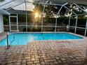 A refreshing screened-in pool with a brick paved patio, with sunset view over backyard at 1039 Greenturf Rd, Spring Hill, FL 34608